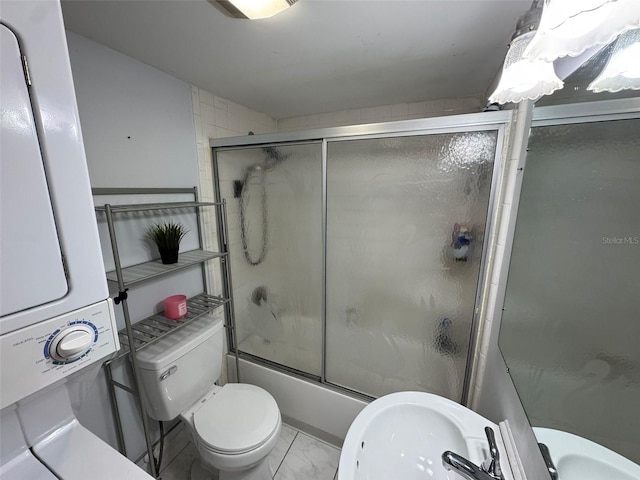 bathroom with stacked washer / drying machine, toilet, and shower / bath combination with glass door