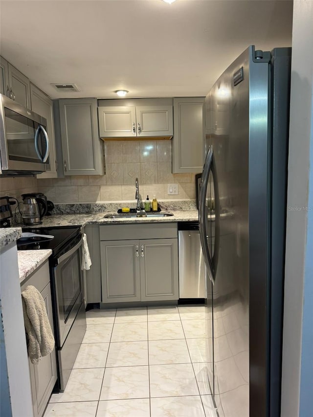 kitchen featuring gray cabinets, stainless steel appliances, backsplash, light stone countertops, and sink