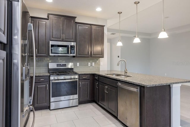 kitchen featuring kitchen peninsula, appliances with stainless steel finishes, hanging light fixtures, light stone counters, and sink