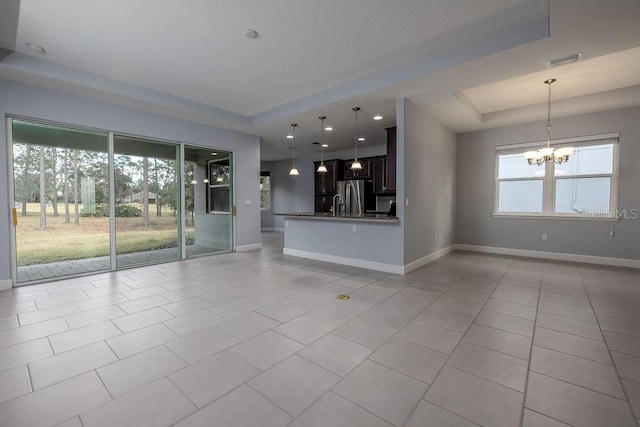 unfurnished living room with light tile patterned floors, plenty of natural light, a tray ceiling, and a chandelier