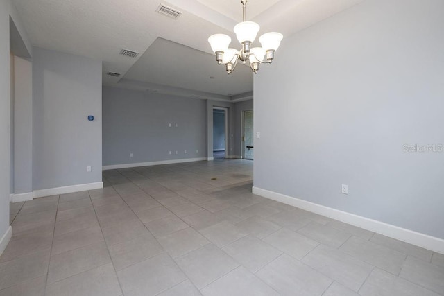 tiled empty room featuring a raised ceiling and a chandelier