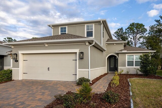 traditional-style home featuring an attached garage, decorative driveway, and stucco siding