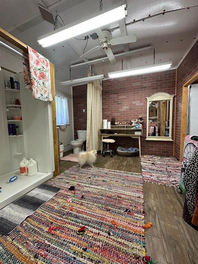 miscellaneous room featuring ceiling fan, dark hardwood / wood-style flooring, and brick wall