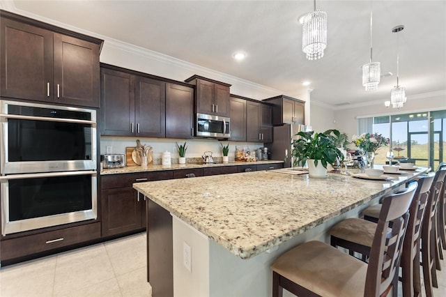 kitchen featuring pendant lighting, an inviting chandelier, a kitchen island with sink, appliances with stainless steel finishes, and light stone counters