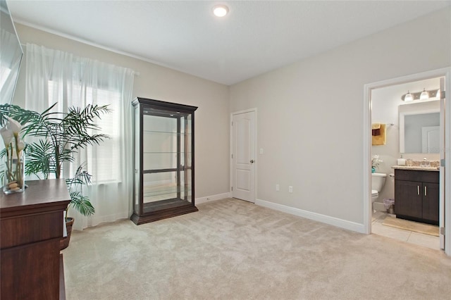 bedroom with baseboards, ensuite bathroom, a sink, and light colored carpet