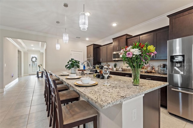 kitchen featuring light tile patterned floors, a kitchen island with sink, stainless steel appliances, a breakfast bar, and dark brown cabinets