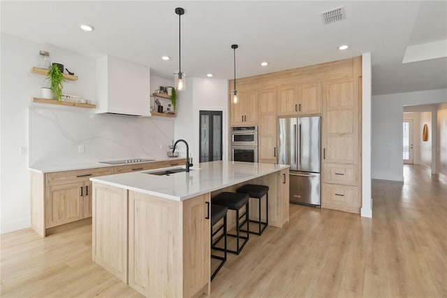 kitchen with sink, light wood-type flooring, a kitchen island with sink, stainless steel appliances, and light brown cabinetry