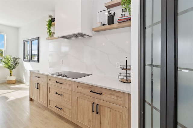 kitchen featuring light brown cabinets, backsplash, black electric cooktop, light wood-type flooring, and custom range hood