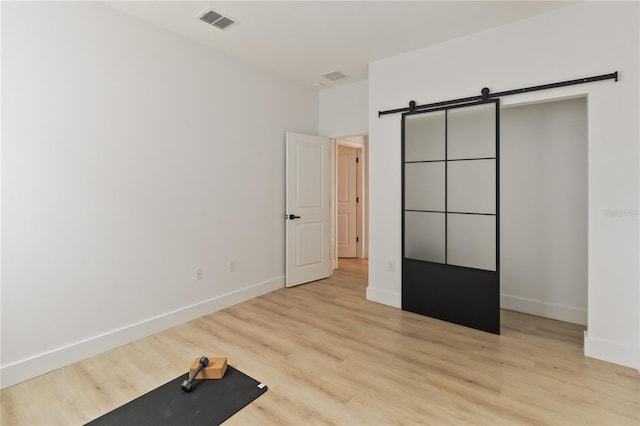 unfurnished bedroom with a barn door and light wood-type flooring