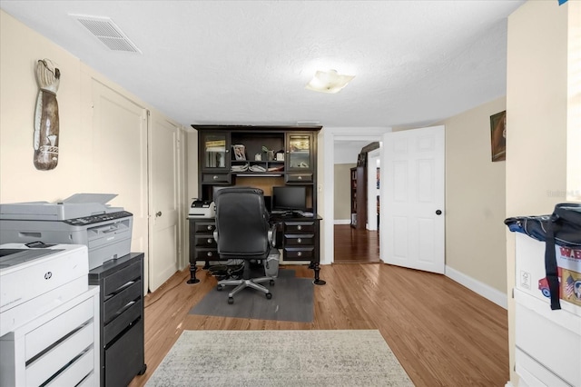 home office featuring light wood-style flooring, a textured ceiling, visible vents, and baseboards