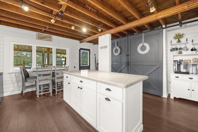 kitchen featuring light stone counters, dark wood finished floors, white cabinets, a kitchen island, and beamed ceiling