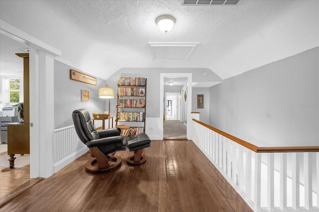 sitting room with vaulted ceiling, hardwood / wood-style floors, visible vents, and attic access