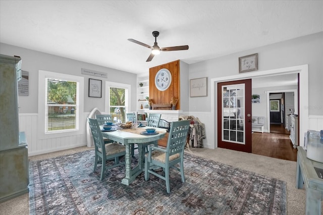 carpeted dining space with a wainscoted wall and a ceiling fan