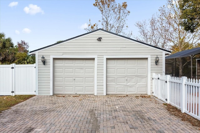 garage featuring decorative driveway, a gate, and fence