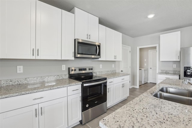 kitchen with stainless steel appliances, independent washer and dryer, white cabinets, and a sink