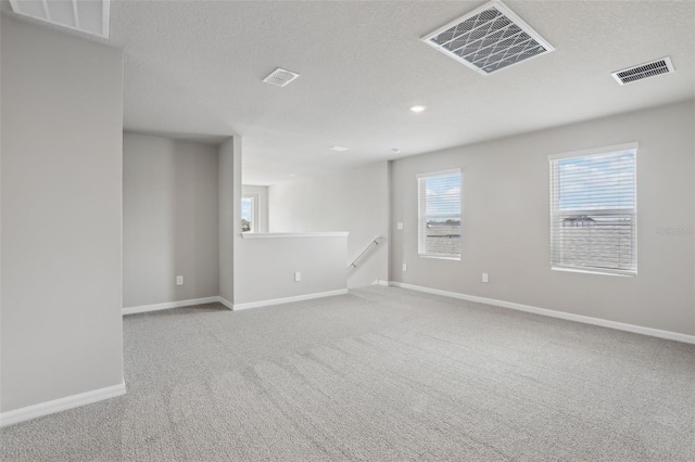 carpeted spare room with a textured ceiling, visible vents, and baseboards