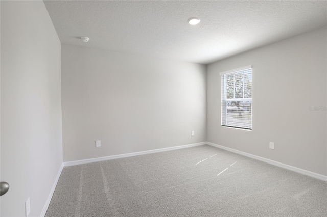 spare room featuring light carpet, a textured ceiling, and baseboards