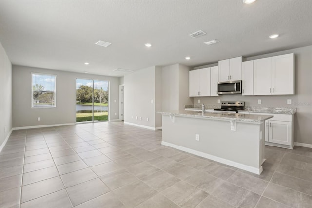 kitchen featuring light tile patterned floors, a center island with sink, stainless steel appliances, and open floor plan