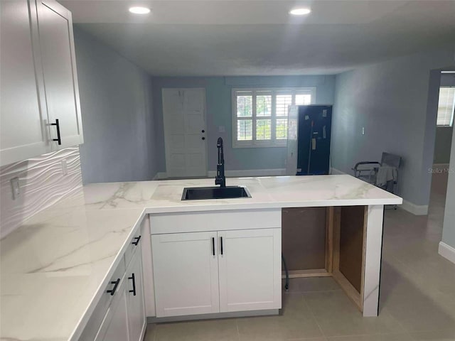 kitchen with light stone countertops, sink, white cabinetry, and kitchen peninsula