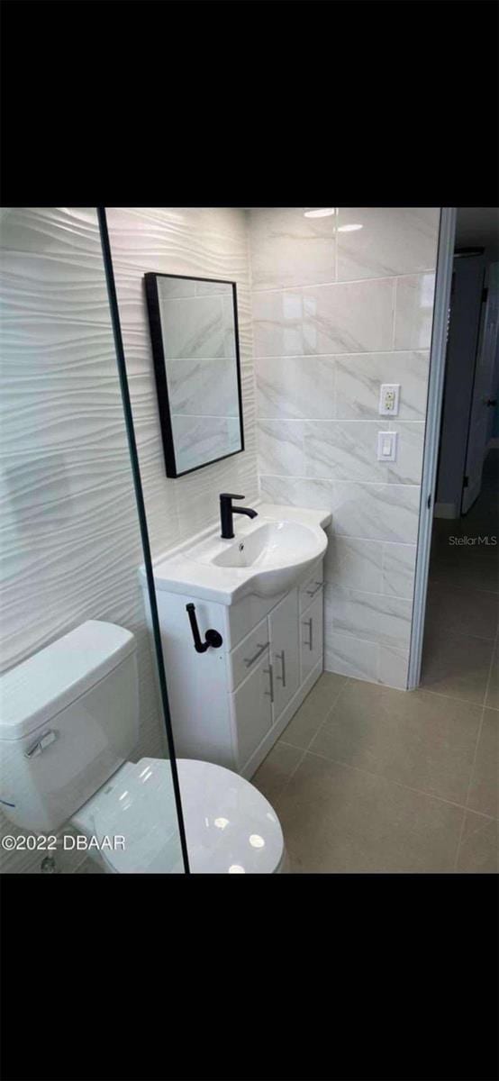 bathroom with tile patterned floors, tile walls, toilet, and vanity