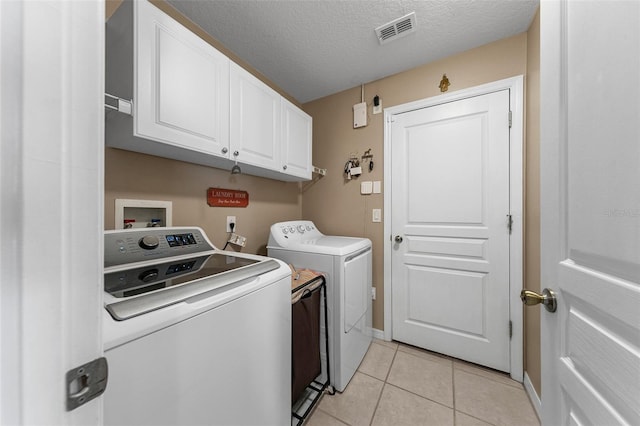 clothes washing area with cabinets, light tile patterned floors, a textured ceiling, and independent washer and dryer