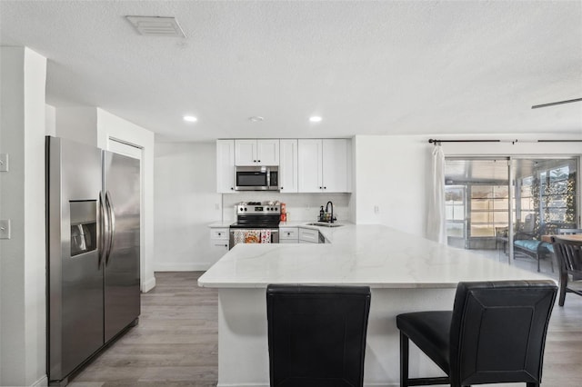 kitchen with white cabinets, appliances with stainless steel finishes, backsplash, kitchen peninsula, and light hardwood / wood-style flooring