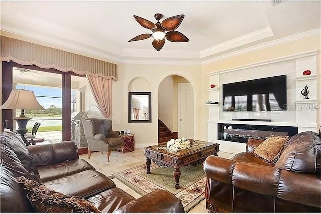 living room with ceiling fan, crown molding, a tray ceiling, and built in shelves