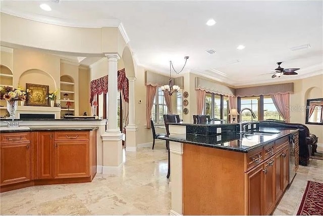 kitchen with an island with sink, built in shelves, dark stone countertops, ceiling fan with notable chandelier, and sink