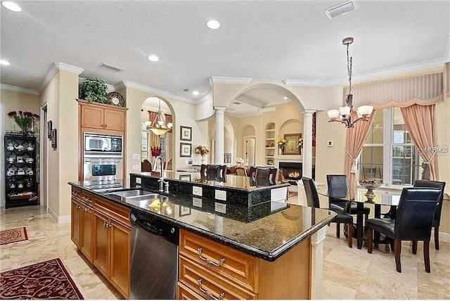 kitchen with an inviting chandelier, an island with sink, appliances with stainless steel finishes, dark stone countertops, and built in shelves