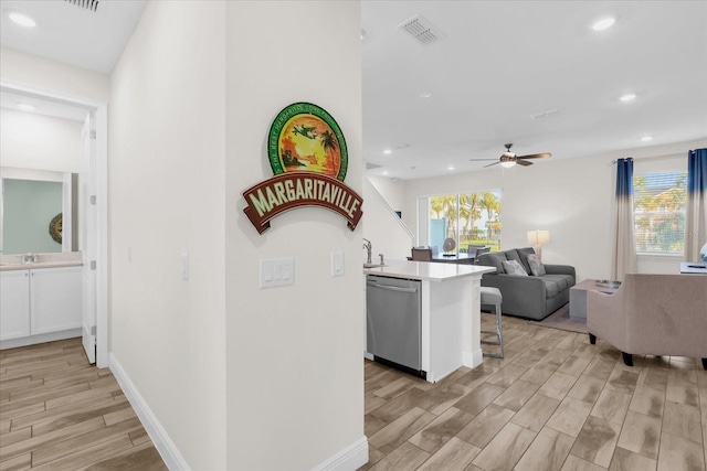 kitchen with white cabinets, dishwasher, kitchen peninsula, ceiling fan, and a breakfast bar area