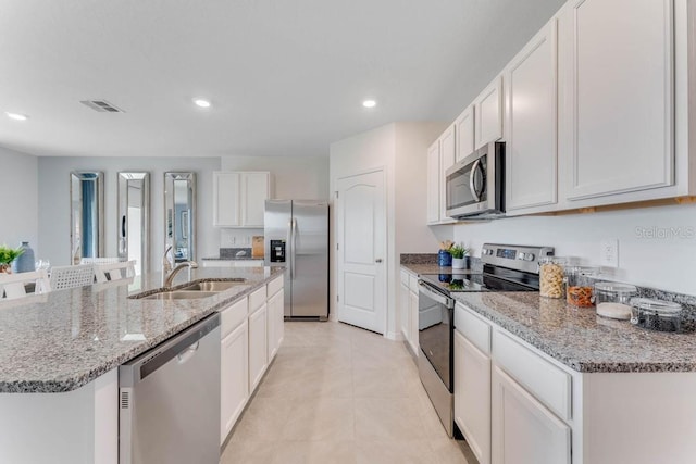 kitchen with white cabinets, stainless steel appliances, sink, a kitchen island with sink, and light tile patterned flooring