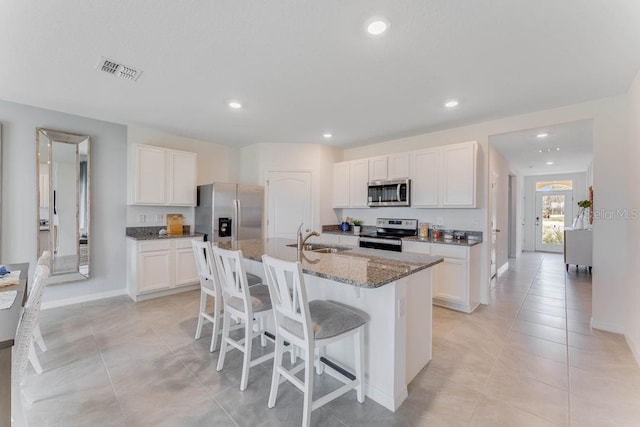 kitchen with stainless steel appliances, sink, white cabinets, and an island with sink