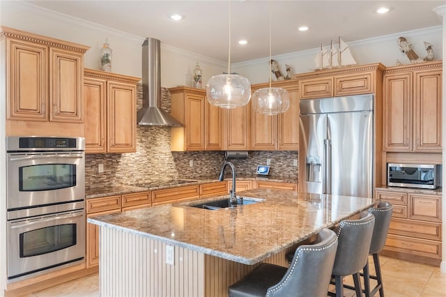 kitchen with decorative backsplash, sink, an island with sink, stainless steel appliances, and wall chimney exhaust hood