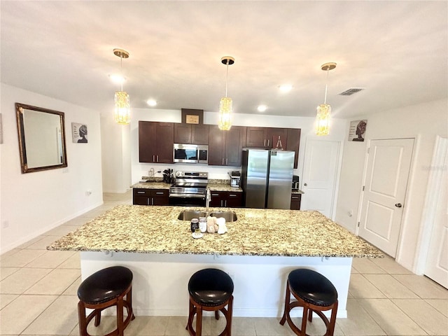 kitchen featuring sink, hanging light fixtures, appliances with stainless steel finishes, and a center island with sink