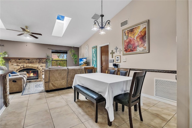 dining space featuring a brick fireplace, light tile patterned floors, lofted ceiling, and ceiling fan with notable chandelier