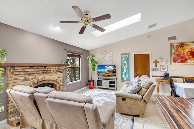 living room with vaulted ceiling with skylight, a textured ceiling, ceiling fan, light tile patterned flooring, and a brick fireplace