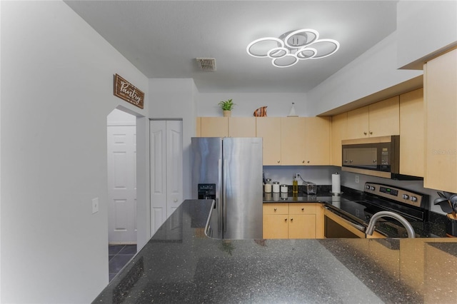 kitchen with light brown cabinets, stainless steel appliances, and dark stone countertops