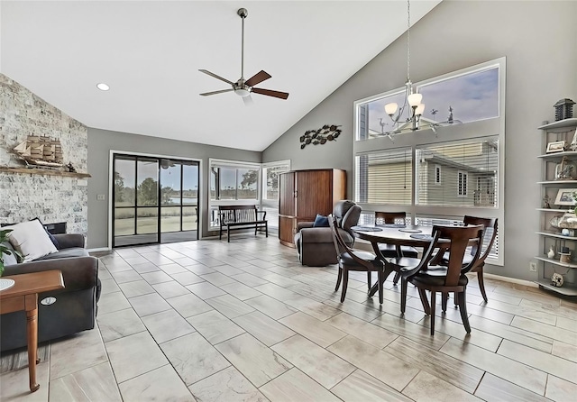 dining room with high vaulted ceiling, a stone fireplace, and ceiling fan with notable chandelier