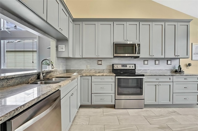 kitchen featuring light stone countertops, gray cabinets, stainless steel appliances, and sink