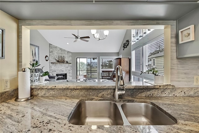 kitchen with light stone countertops, lofted ceiling, sink, a large fireplace, and ceiling fan