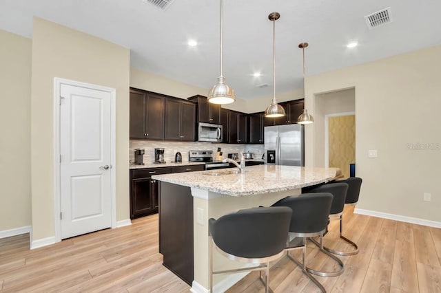 kitchen featuring appliances with stainless steel finishes, decorative light fixtures, sink, light stone countertops, and a center island with sink