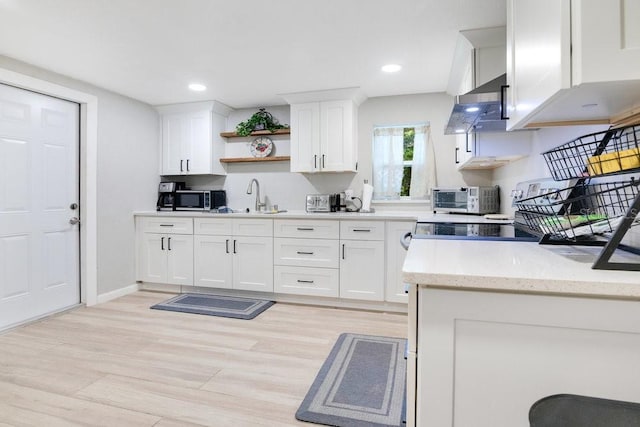 kitchen with light stone counters, wall chimney exhaust hood, sink, and white cabinets