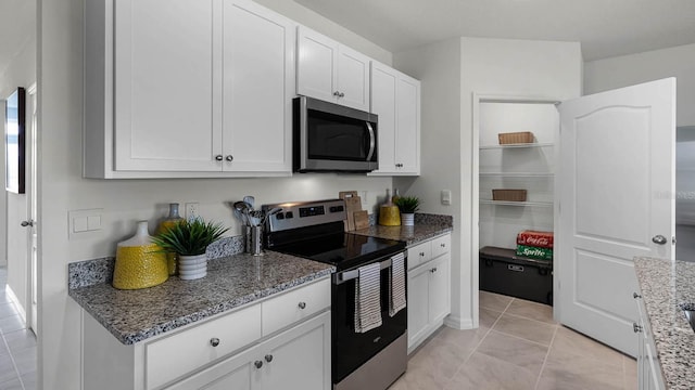 kitchen featuring appliances with stainless steel finishes, light tile patterned flooring, stone counters, and white cabinetry