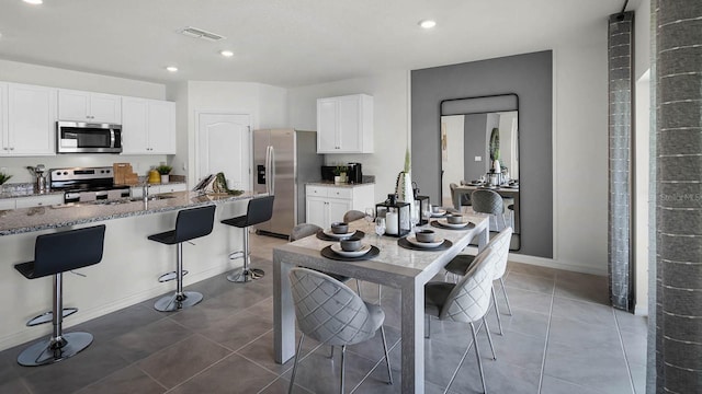 kitchen with stone counters, appliances with stainless steel finishes, white cabinetry, and a kitchen breakfast bar