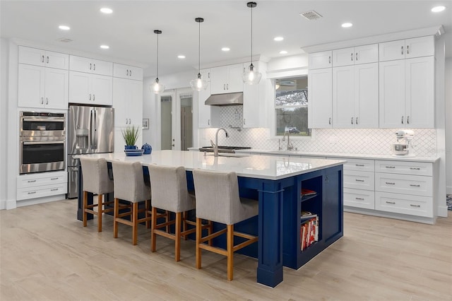 kitchen featuring a breakfast bar, white cabinetry, a center island with sink, appliances with stainless steel finishes, and pendant lighting