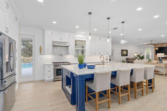 kitchen with sink, white cabinetry, decorative light fixtures, stainless steel appliances, and a kitchen island with sink