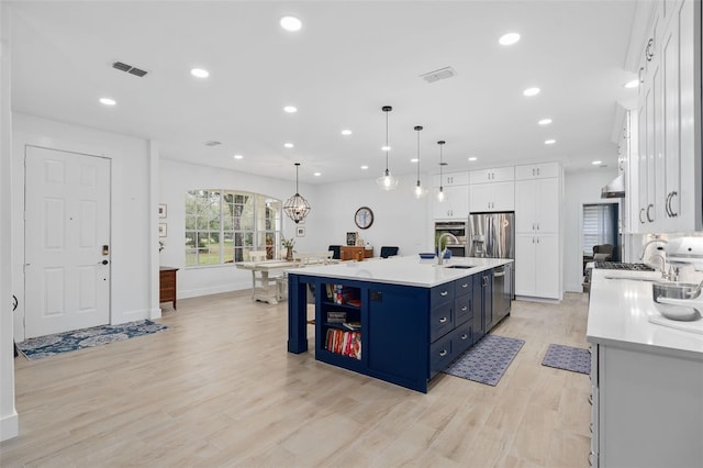 kitchen featuring blue cabinetry, sink, white cabinetry, an island with sink, and pendant lighting