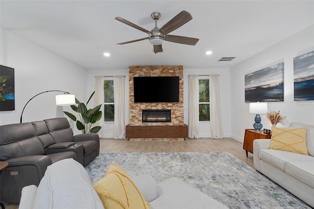 living room with ceiling fan, a stone fireplace, and light hardwood / wood-style floors