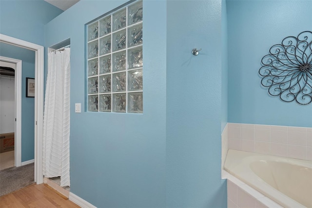 bathroom with wood-type flooring and a relaxing tiled tub