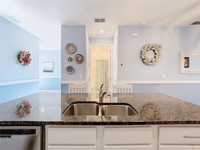 kitchen featuring stainless steel dishwasher, white cabinets, sink, and dark stone countertops